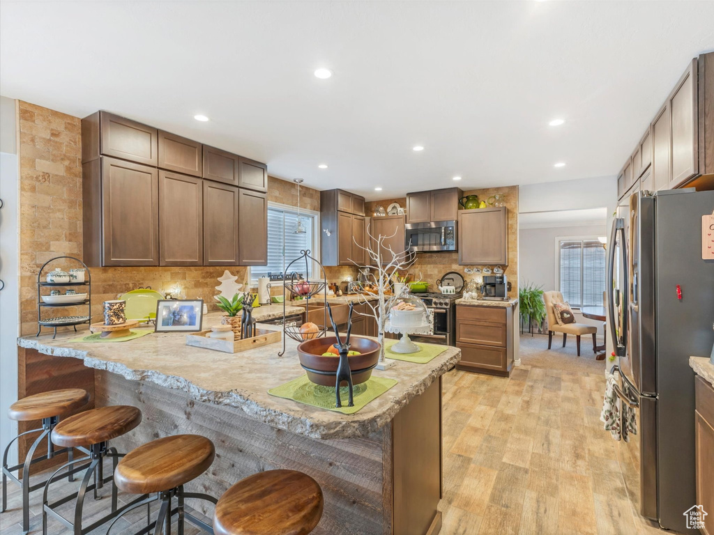 Kitchen with tasteful backsplash, light wood finished floors, a breakfast bar, stainless steel appliances, and recessed lighting