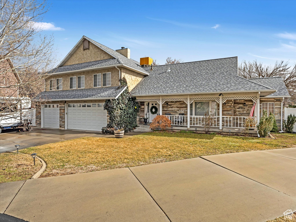 View of front of home featuring a garage, covered porch, a front yard, a shingled roof, and driveway