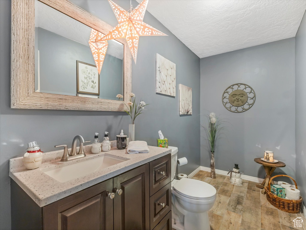Half bathroom with a textured ceiling, wood finished floors, vanity, baseboards, and toilet
