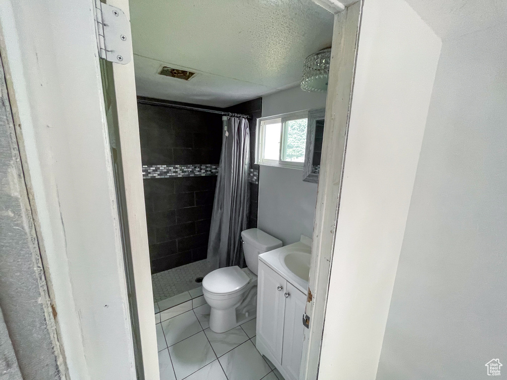Full bath featuring vanity, a textured ceiling, toilet, and tiled shower