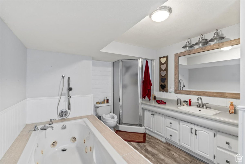 Bathroom with toilet, a tub with jets, wainscoting, vanity, and wood finished floors