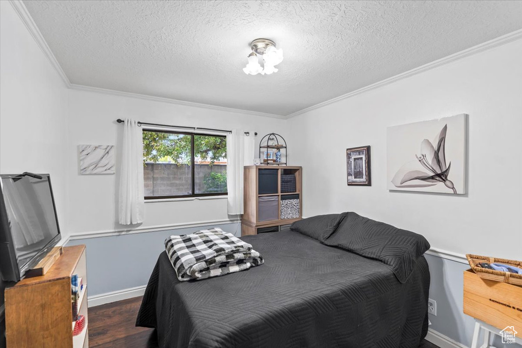 Bedroom with crown molding, a textured ceiling, wood finished floors, and baseboards