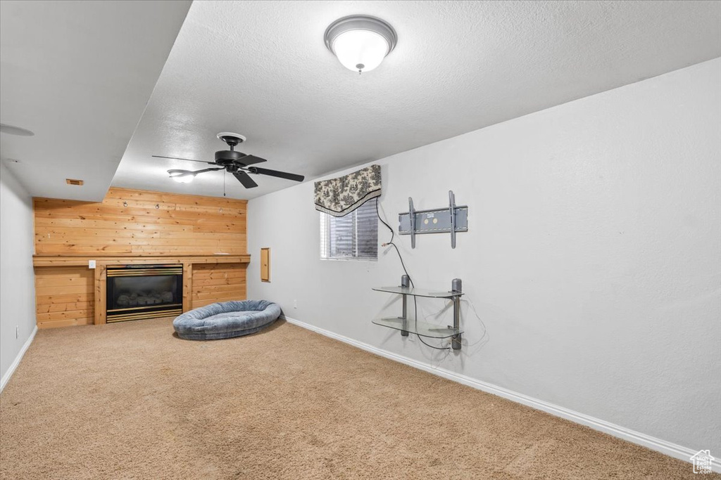 Unfurnished living room with ceiling fan, a glass covered fireplace, carpet floors, wooden walls, and baseboards
