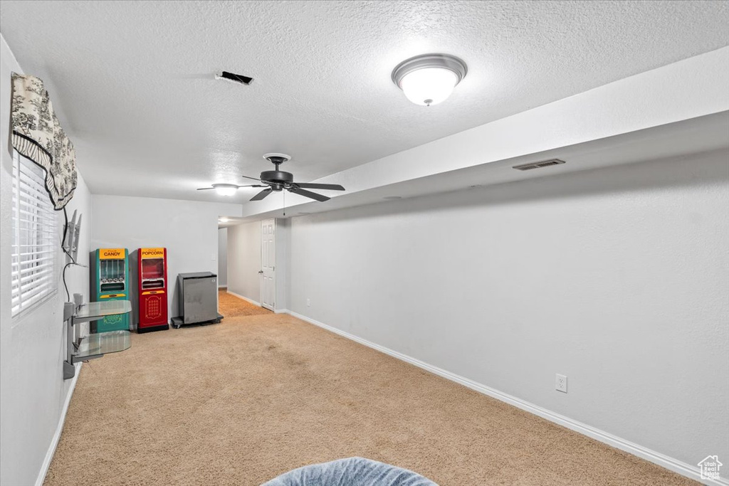 Below grade area featuring light colored carpet, baseboards, a textured ceiling, and a ceiling fan