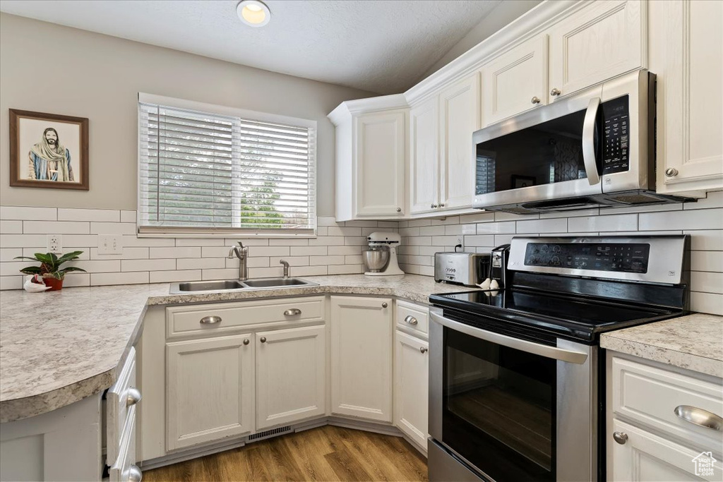 Kitchen featuring light countertops, appliances with stainless steel finishes, decorative backsplash, and a sink
