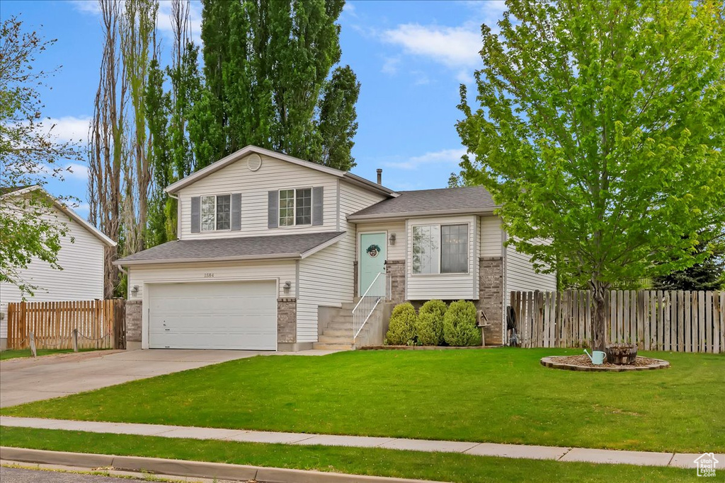 Split level home featuring fence, a garage, concrete driveway, and a front yard