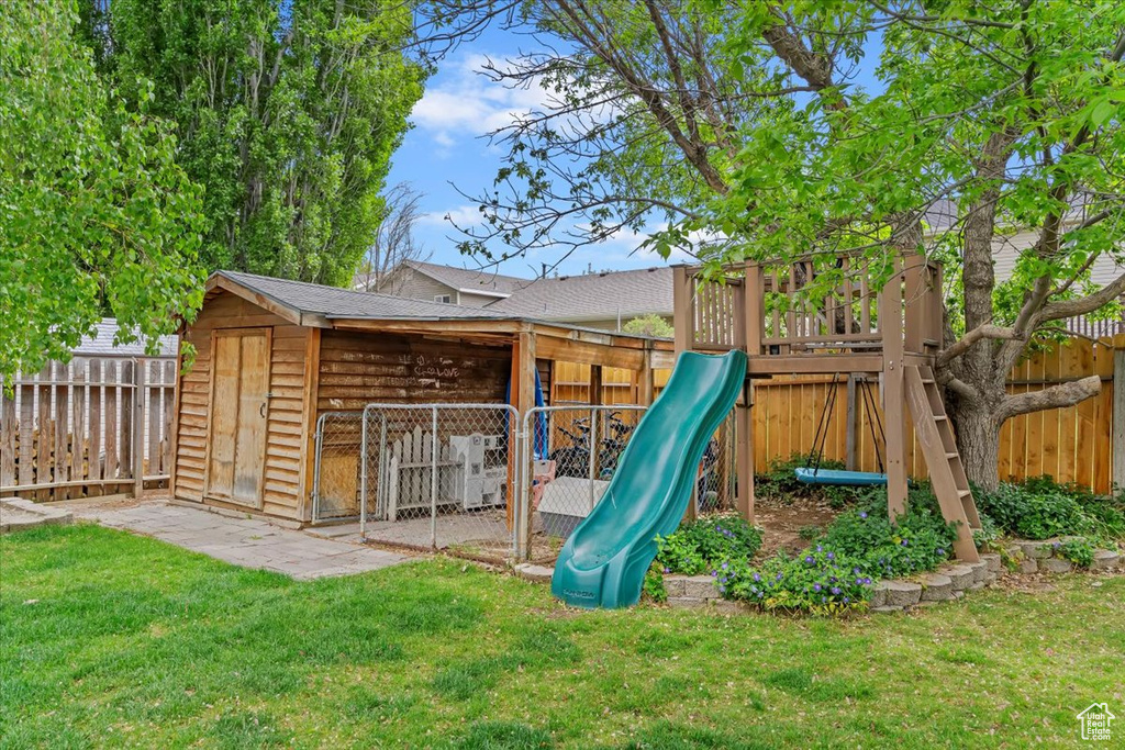 View of jungle gym with a fenced backyard, a storage shed, an outbuilding, and a lawn