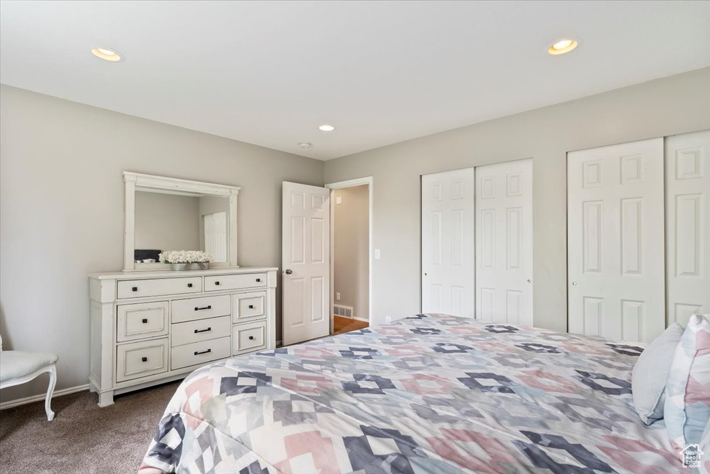 Bedroom with two closets, visible vents, dark carpet, and recessed lighting