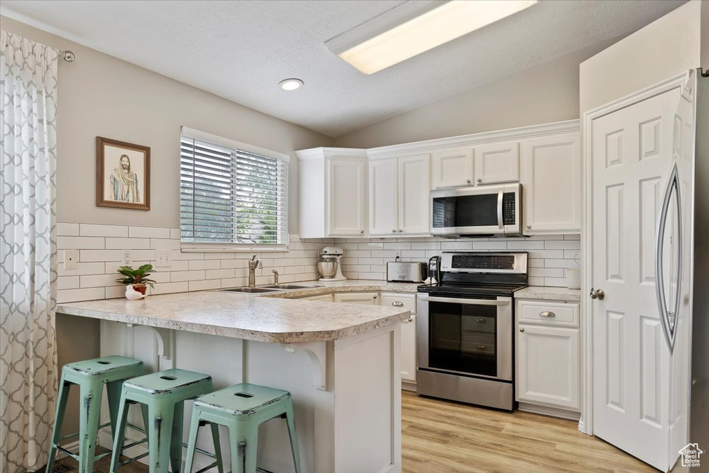 Kitchen featuring a peninsula, vaulted ceiling, backsplash, white cabinets, and appliances with stainless steel finishes
