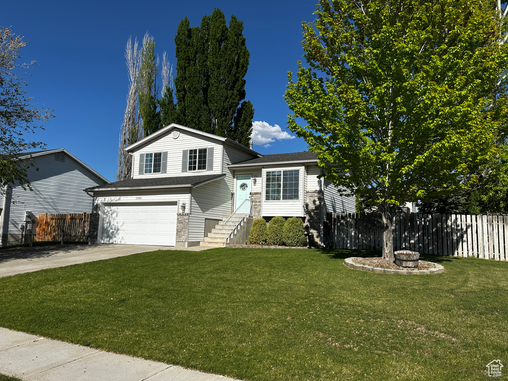 Tri-level home featuring fence, driveway, a front lawn, and a garage