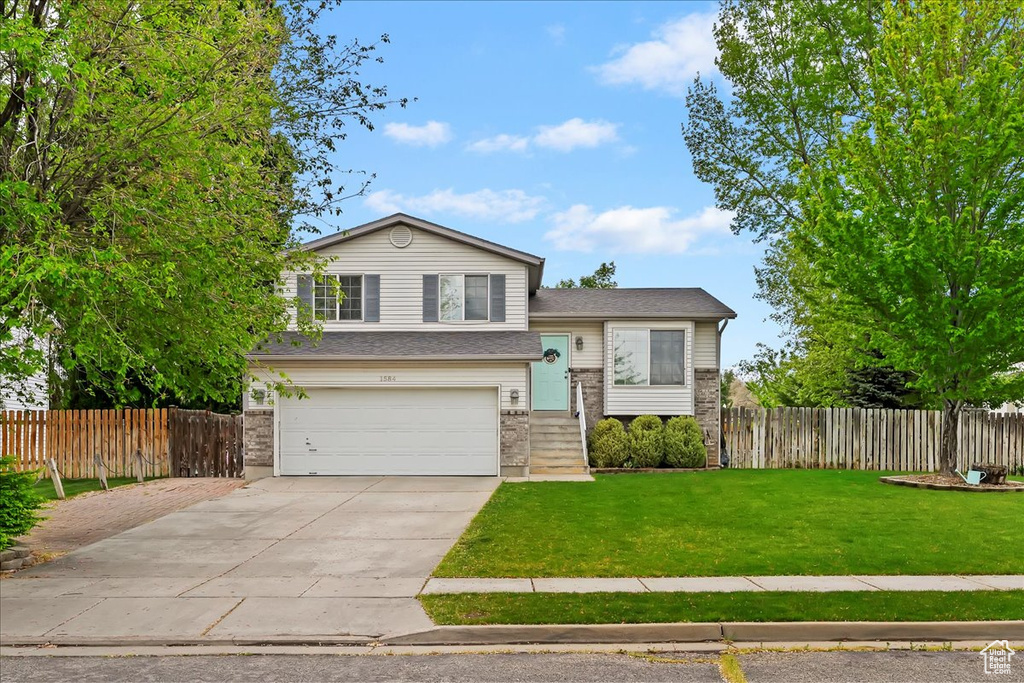 Split level home with concrete driveway, an attached garage, fence, and a front yard