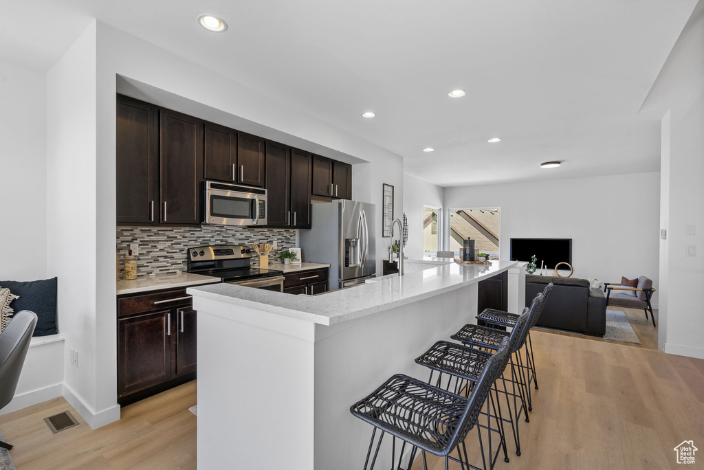 Kitchen with backsplash, open floor plan, a breakfast bar, stainless steel appliances, and light wood-style flooring