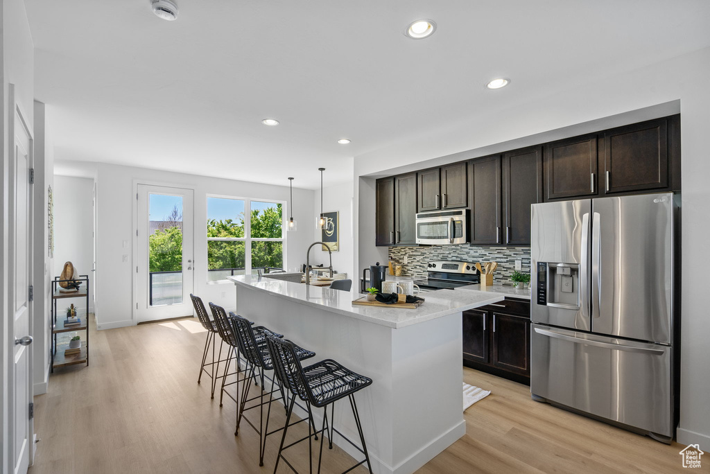 Kitchen featuring appliances with stainless steel finishes, a breakfast bar area, light countertops, light wood-style flooring, and decorative backsplash