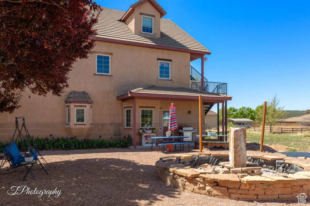 Rear view of property with a fire pit, stucco siding, a balcony, and fence