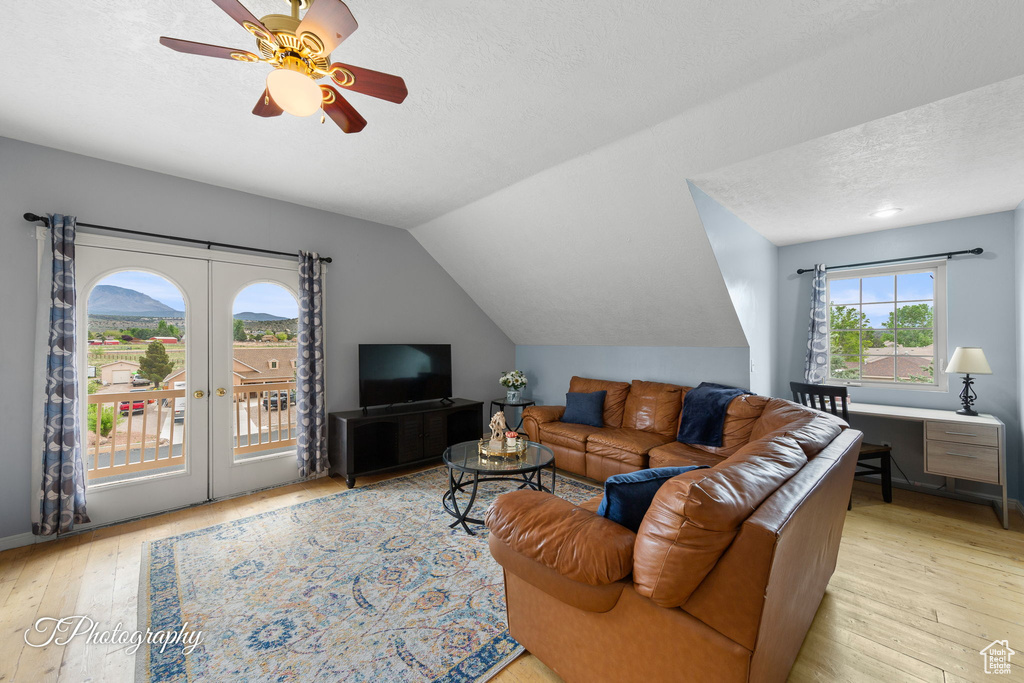 Living room with lofted ceiling, a textured ceiling, french doors, a ceiling fan, and light wood-style flooring