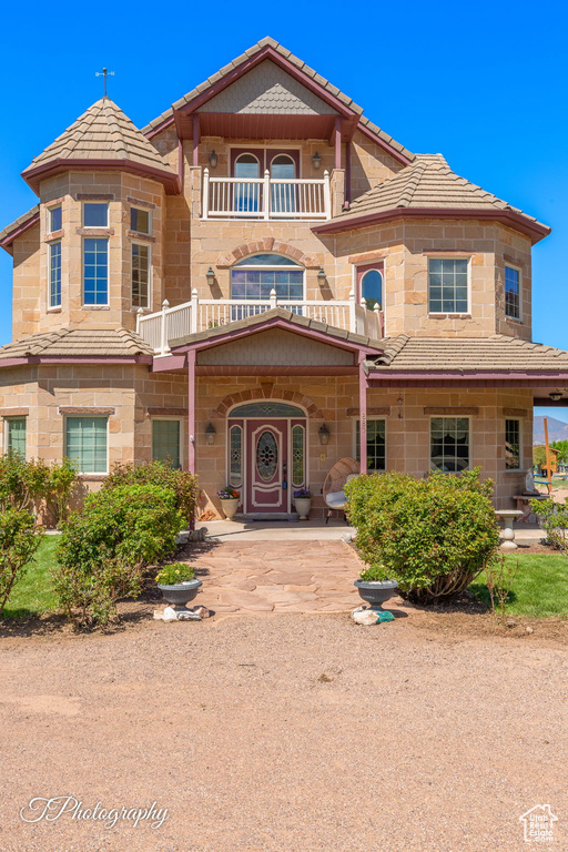 View of front of property with a tile roof, a balcony, and stone siding