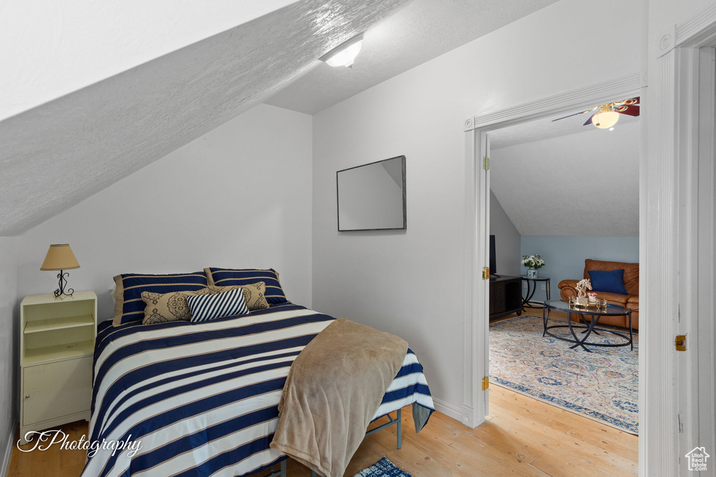 Bedroom featuring baseboards, a textured ceiling, wood finished floors, and lofted ceiling