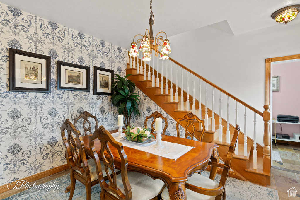 Dining room featuring stairs, wallpapered walls, an inviting chandelier, and baseboards