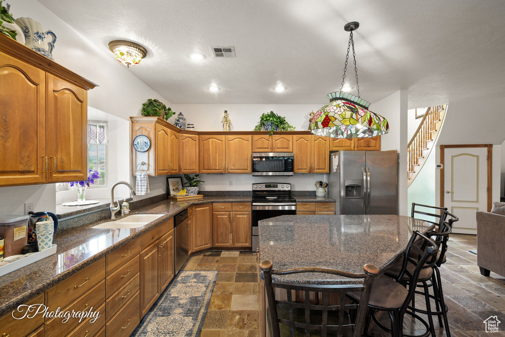 Kitchen with brown cabinetry, visible vents, a sink, stone tile flooring, and stainless steel appliances