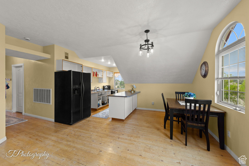 Kitchen with white cabinetry, visible vents, black fridge, and light wood-type flooring