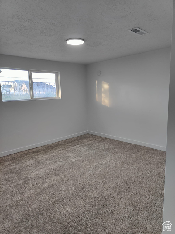 Carpeted spare room featuring a textured ceiling and baseboards