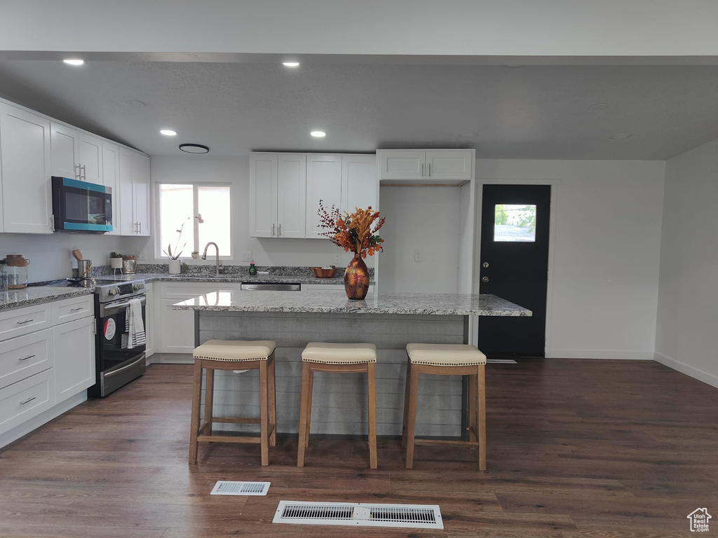 Kitchen with appliances with stainless steel finishes, a center island, a breakfast bar area, white cabinets, and recessed lighting
