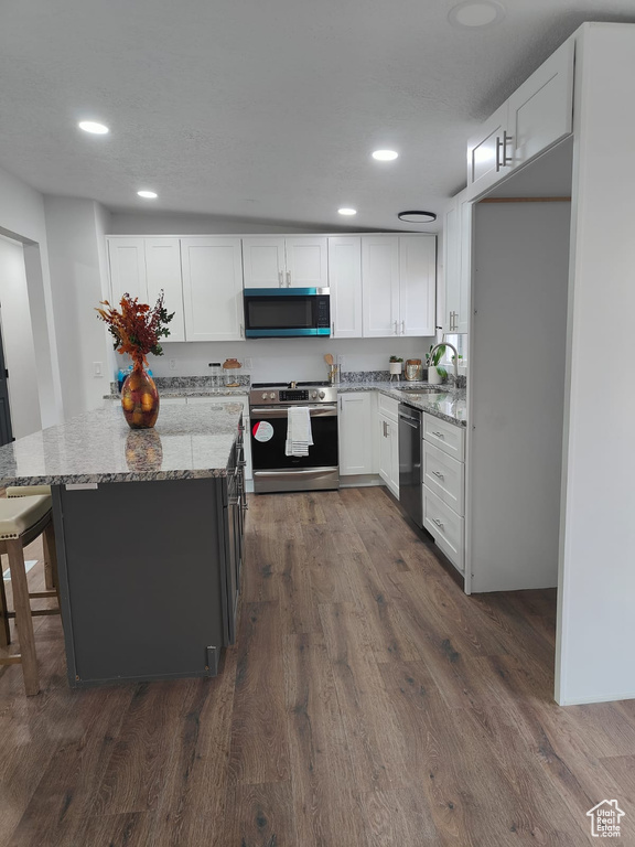 Kitchen with stainless steel appliances, a sink, light stone counters, white cabinets, and recessed lighting
