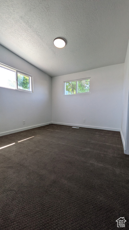 Unfurnished room featuring baseboards, dark carpet, and a textured ceiling