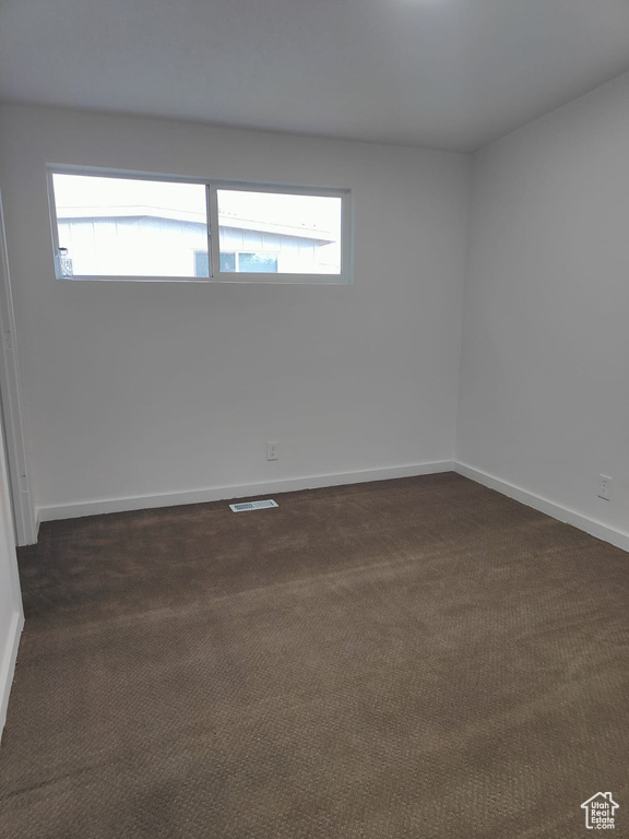 Empty room featuring plenty of natural light, dark colored carpet, and baseboards