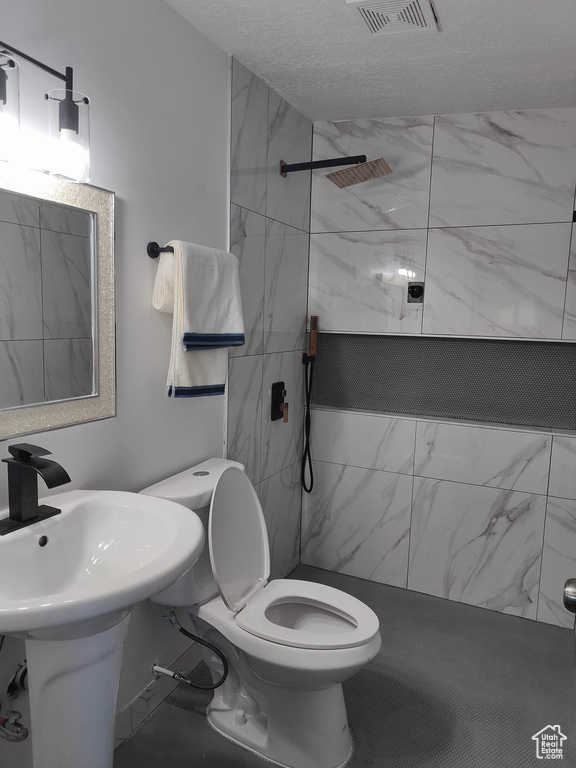 Bathroom with tiled shower, toilet, marble look tiles, a sink, and a textured ceiling