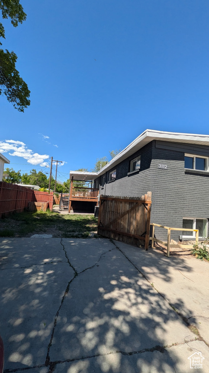 View of property exterior featuring brick siding, fence, a deck, and a patio