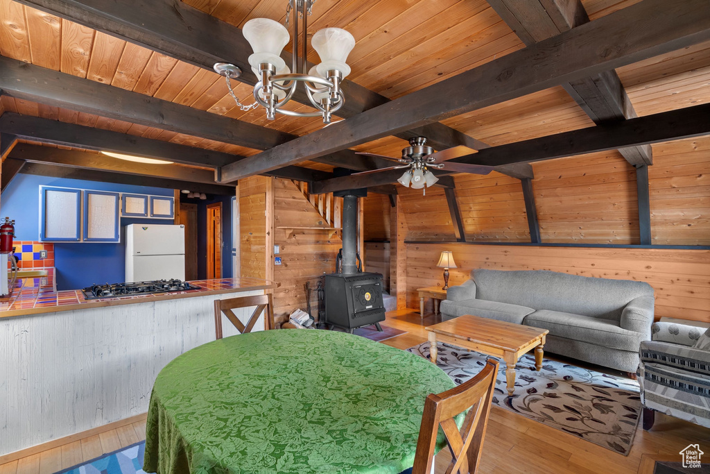 Dining area featuring wood ceiling, a wood stove, beamed ceiling, ceiling fan with notable chandelier, and wooden walls