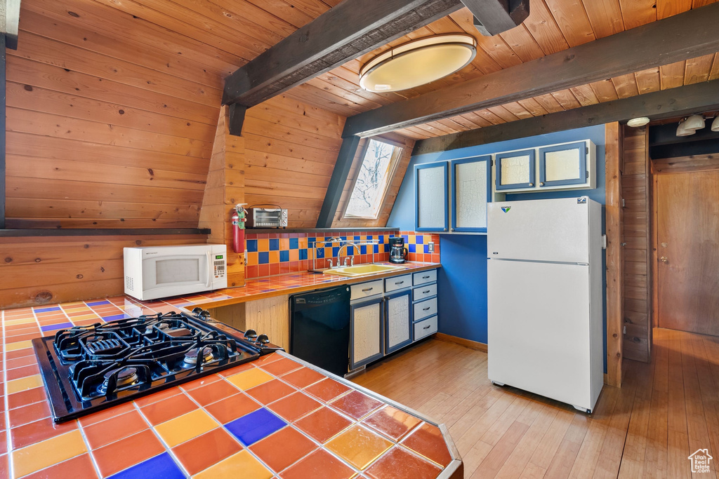 Kitchen with a sink, tile countertops, wooden ceiling, a skylight, and black appliances