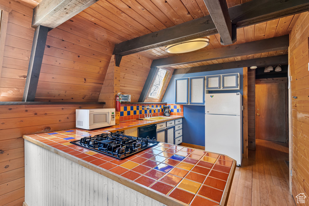 Kitchen featuring tile countertops, wood walls, beamed ceiling, black appliances, and wood-type flooring