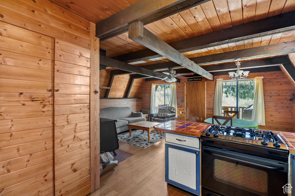 Kitchen with tile countertops, wooden ceiling, beamed ceiling, black range with gas stovetop, and wooden walls