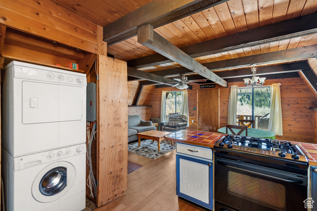 Kitchen with black range with gas cooktop, tile countertops, wood walls, stacked washer and clothes dryer, and a wealth of natural light