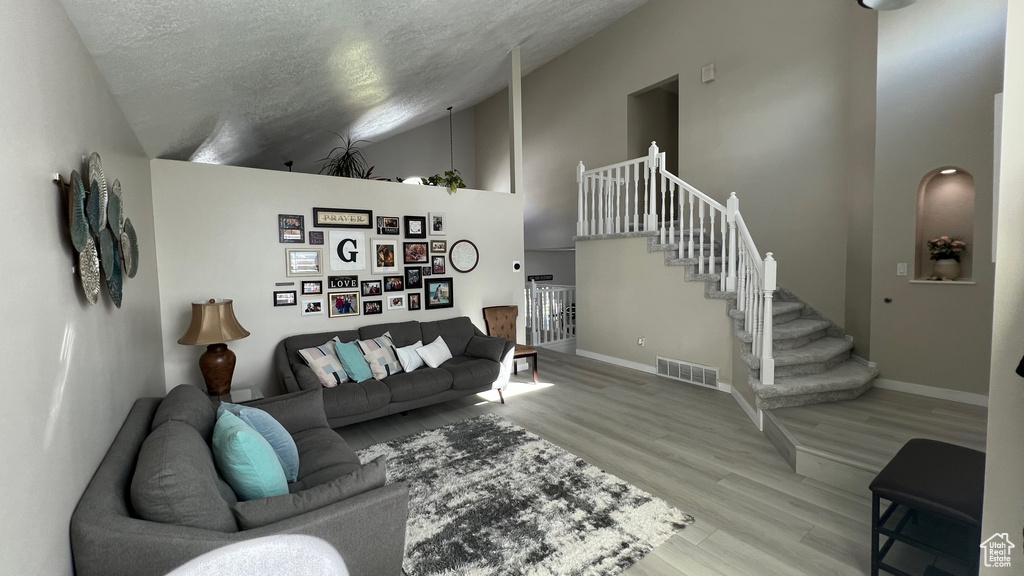 Living room featuring a textured ceiling, visible vents, wood finished floors, baseboards, and stairs