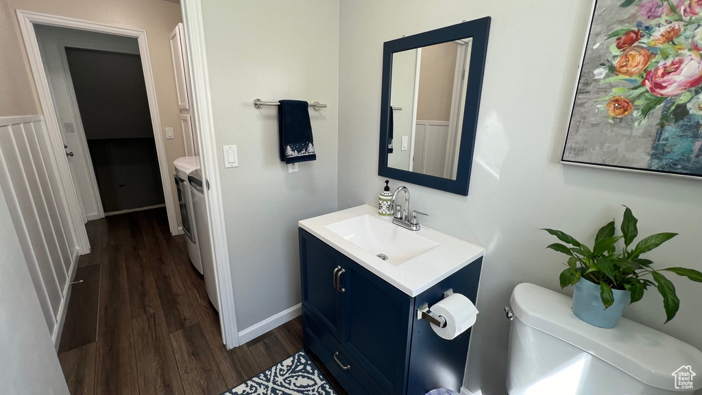 Half bath featuring washing machine and dryer, wood finished floors, vanity, baseboards, and toilet