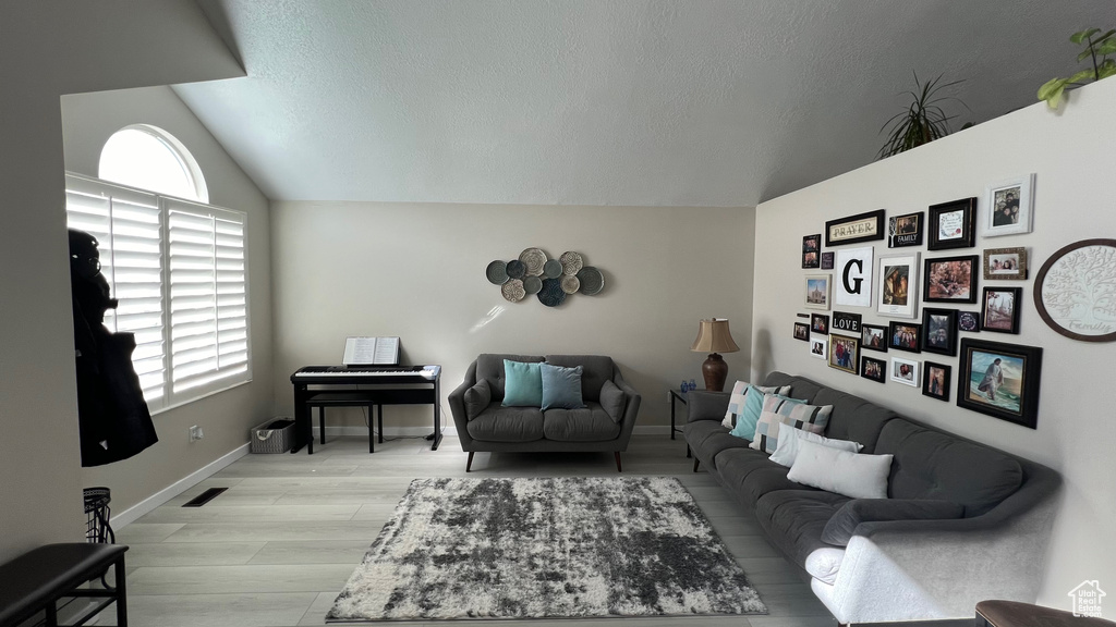 Living room featuring baseboards, light wood-style flooring, vaulted ceiling, and a textured ceiling