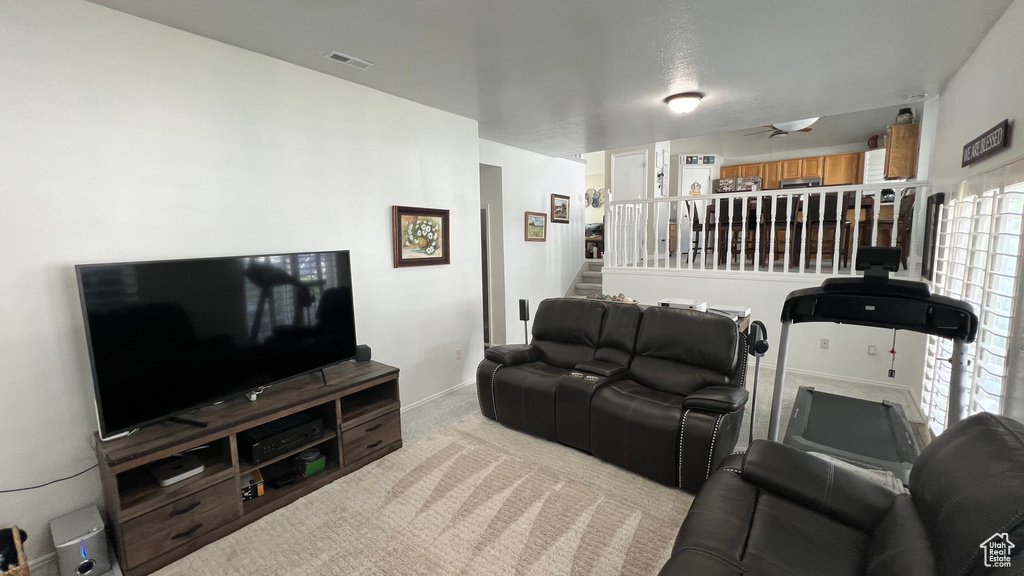 Carpeted living area featuring baseboards, ceiling fan, stairs, and visible vents