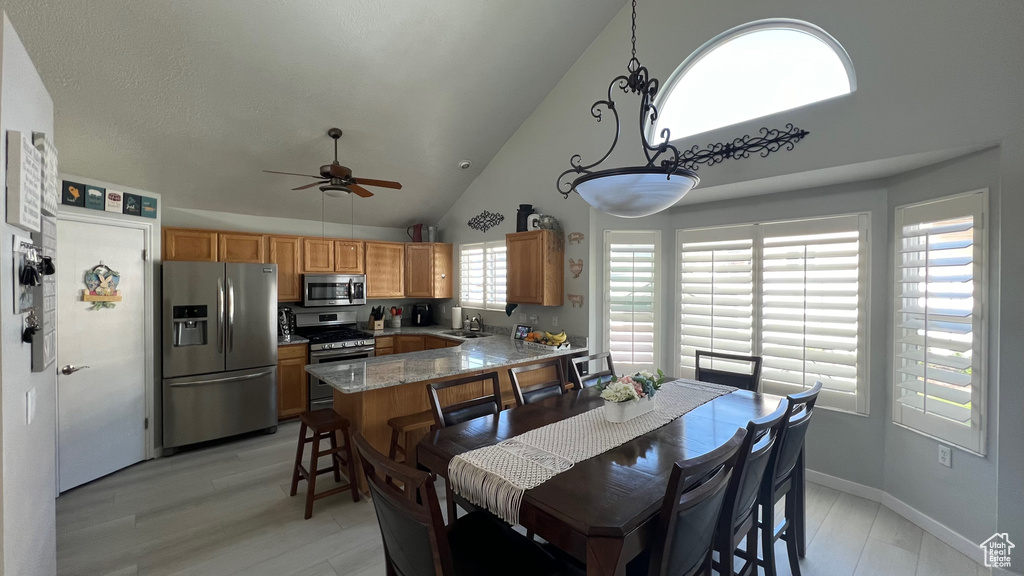 Dining room featuring high vaulted ceiling, baseboards, a ceiling fan, and light wood-style flooring