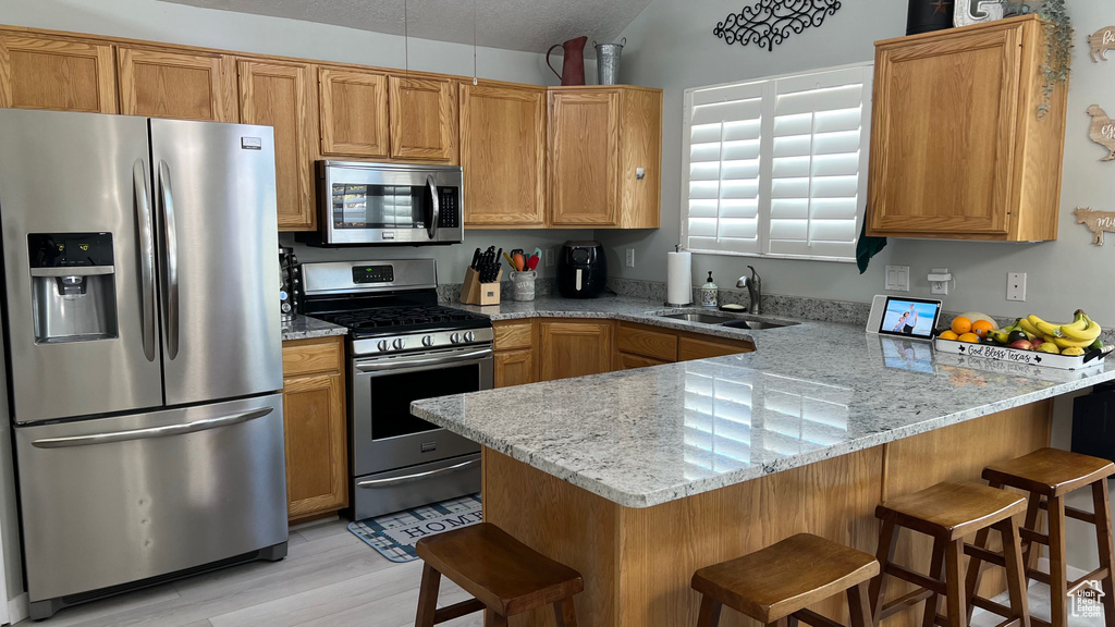 Kitchen with a sink, a peninsula, a breakfast bar, stainless steel appliances, and light wood-style flooring