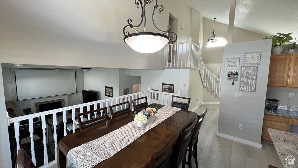 Dining space featuring a fireplace, high vaulted ceiling, baseboards, light wood finished floors, and stairs