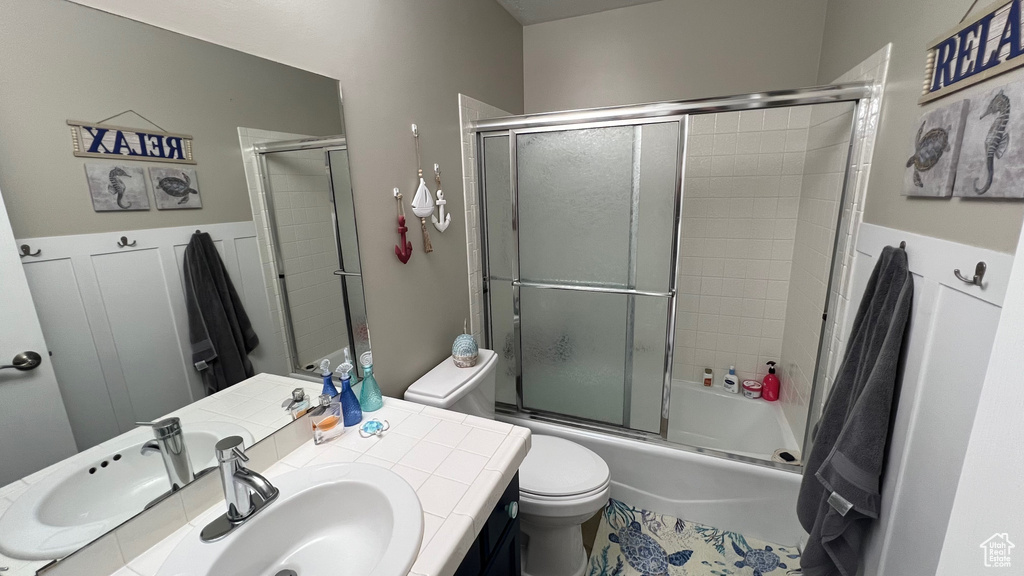 Bathroom featuring toilet, bath / shower combo with glass door, and vanity