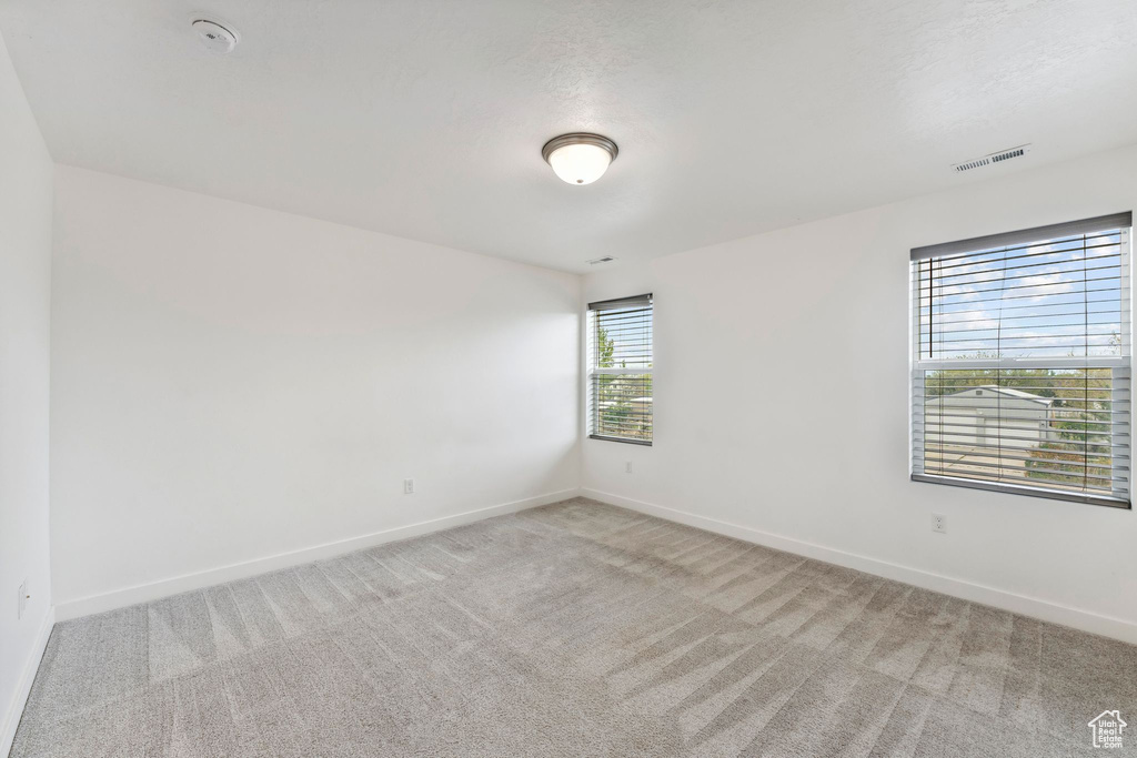 Empty room with baseboards, visible vents, and light carpet