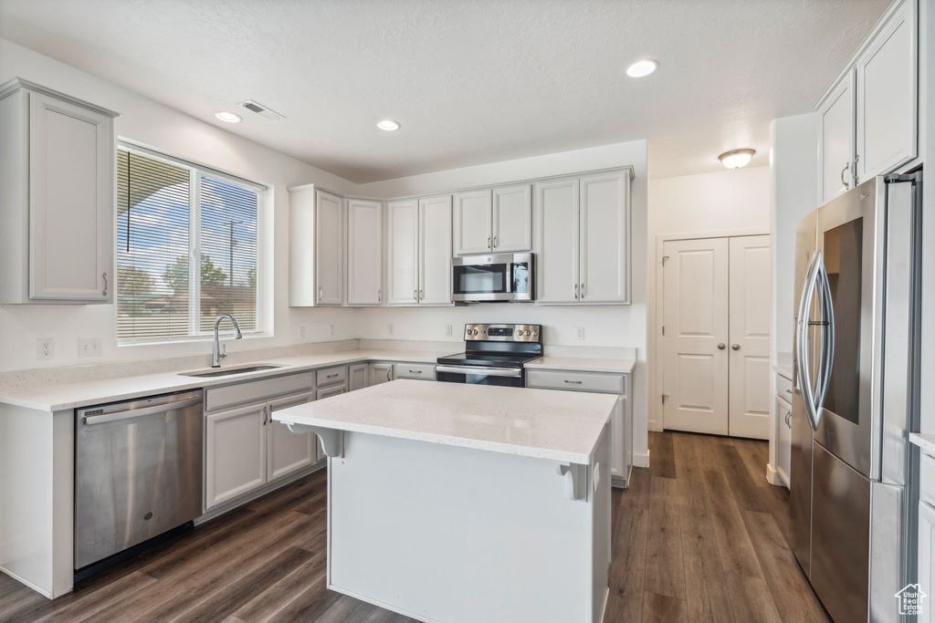 Kitchen featuring visible vents, a center island, a sink, stainless steel appliances, and dark wood-type flooring