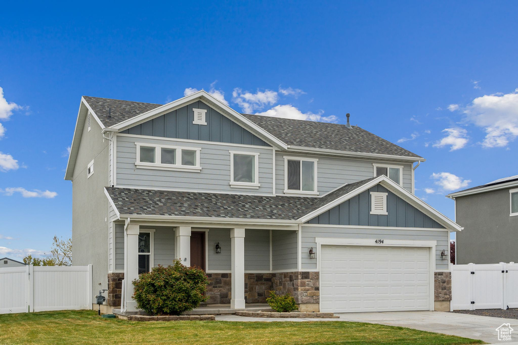 View of front facade with board and batten siding, fence, covered porch, and concrete driveway