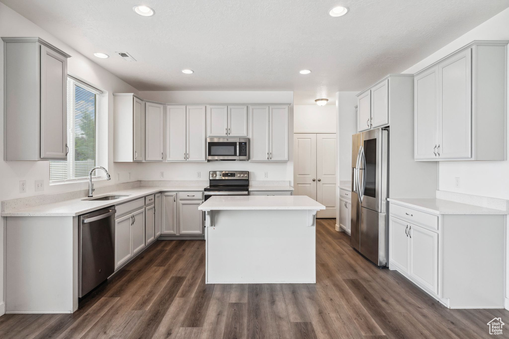 Kitchen with appliances with stainless steel finishes, a sink, light countertops, a center island, and dark wood-style floors