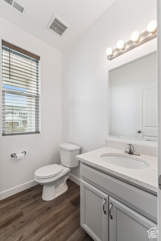 Half bathroom featuring visible vents, vanity, wood finished floors, toilet, and baseboards