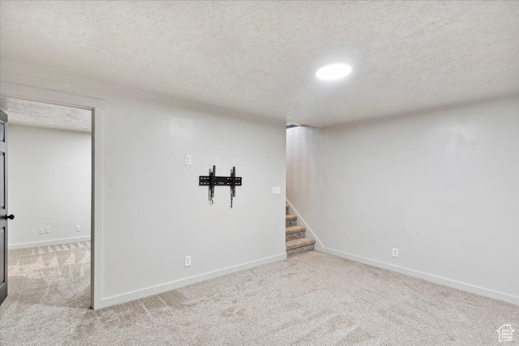 Finished below grade area featuring carpet floors, baseboards, stairs, and a textured ceiling
